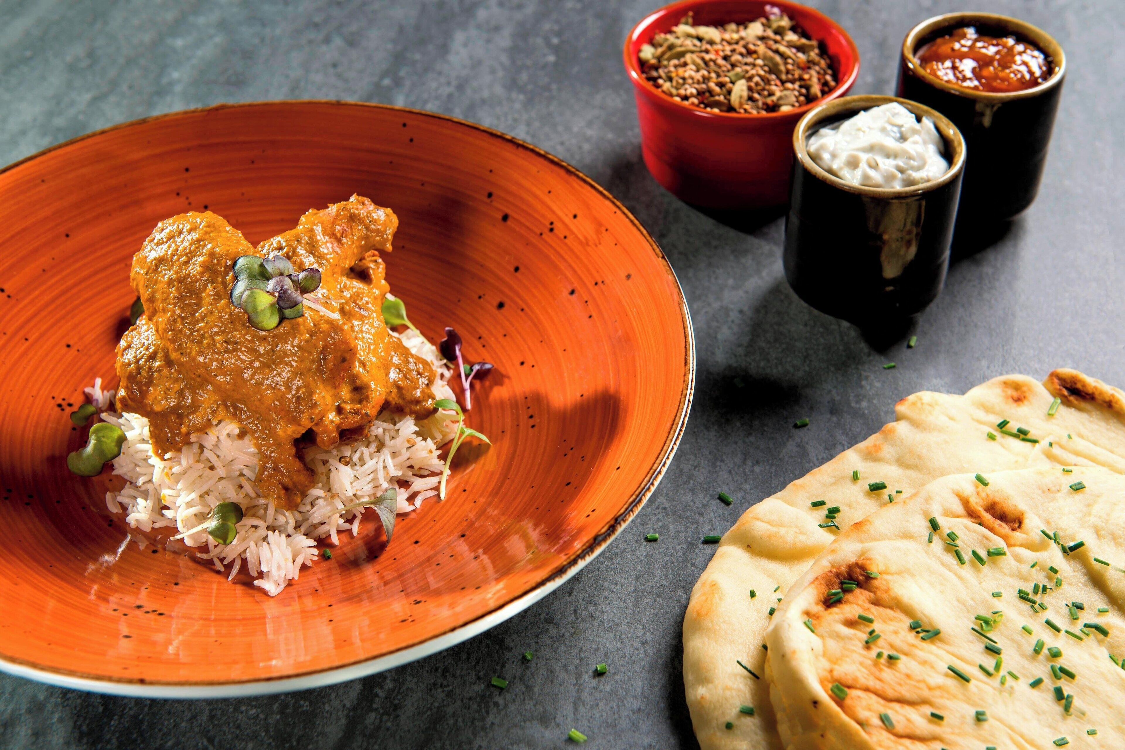 Une assiette de curry de poulet, accompagné de riz et de petits pois, servie avec du pain naan et deux petits bols de chutney.