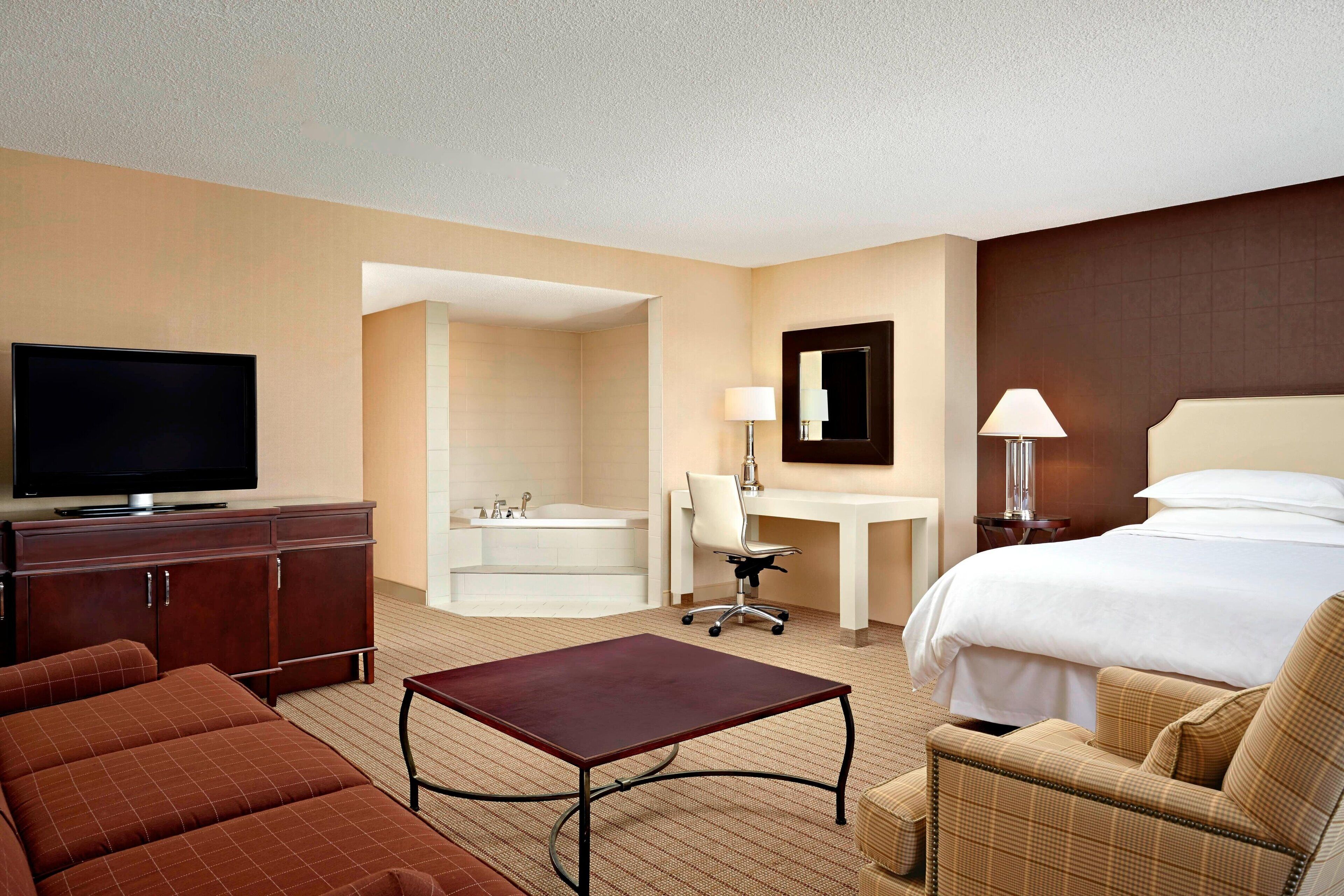 A hotel room with a bed, a desk, a chair, a television, a bathroom, and a small table.