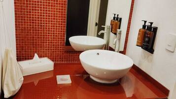 Un baño con pared de azulejos rojos, dos lavamanos, un espejo y toallas.