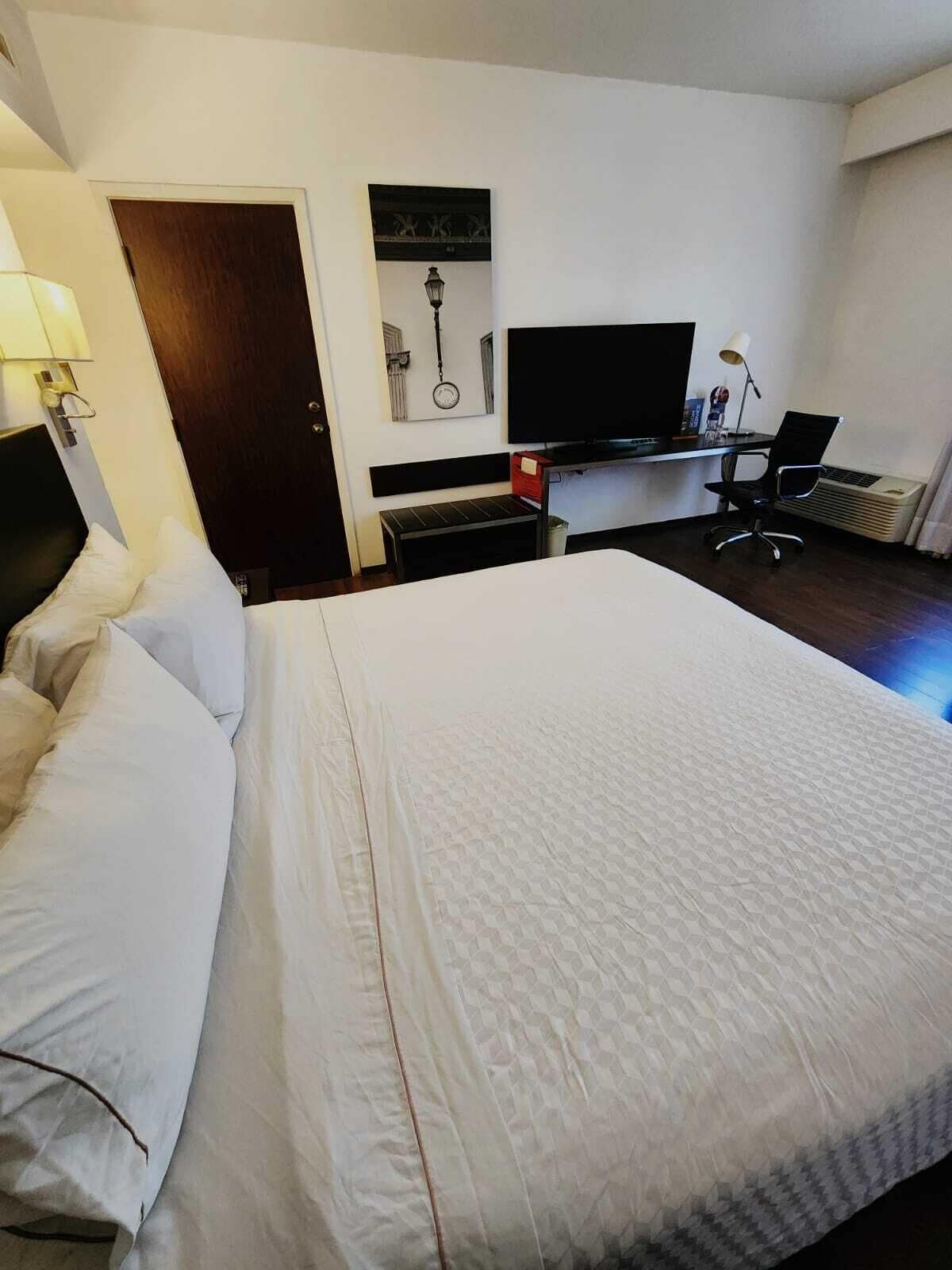 Habitación de hotel con cama, escritorio, computadora, televisor y una silla.