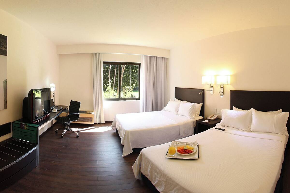A hotel room with two beds, a desk with a computer, a TV, and a breakfast tray.