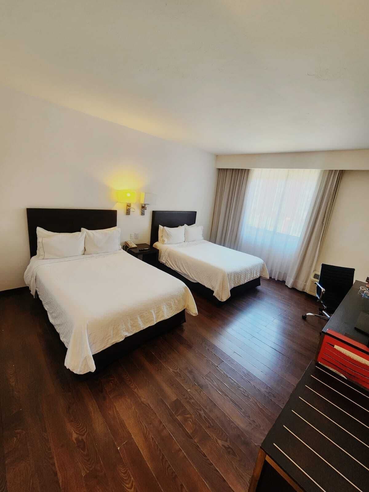 Quarto de hotel com duas camas, uma escrivaninha e uma cadeira.