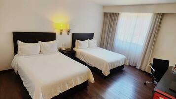 Quarto de hotel com duas camas, uma escrivaninha e uma cadeira.