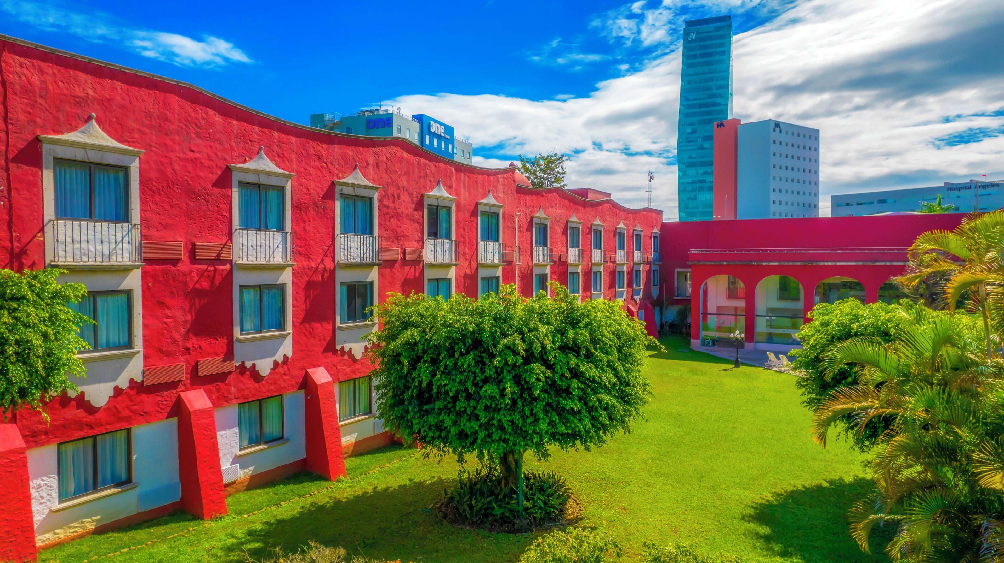 A hotel with red exterior walls, multiple balconies, and a well-maintained lawn.