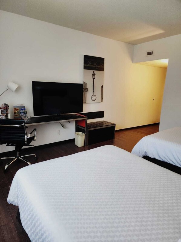 A hotel room with a bed, a desk with a television, a lamp, and a small trash bin.