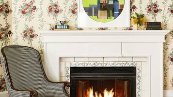 A room with a fireplace, floral wallpaper, a houndstooth patterned chair, and a red and black checkered floor.