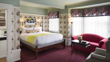 Un dormitorio con una cama, un sillón rojo, una mesita y una estantería.