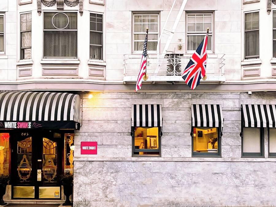 A building facade with a storefront labeled "WHITE SWAN" and two flags, one American and one British.