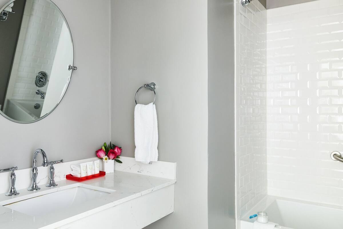 A modern bathroom with a white sink, a round mirror, a towel rack, and a shower area.