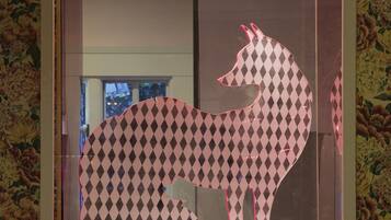 A framed artwork of a stylized animal with a checkered pattern, displayed against a floral wallpaper background.