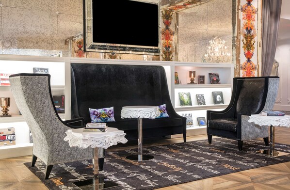 Una sala de estar moderna con un sofá negro, dos sillones, una mesita blanca y un tapete decorativo.