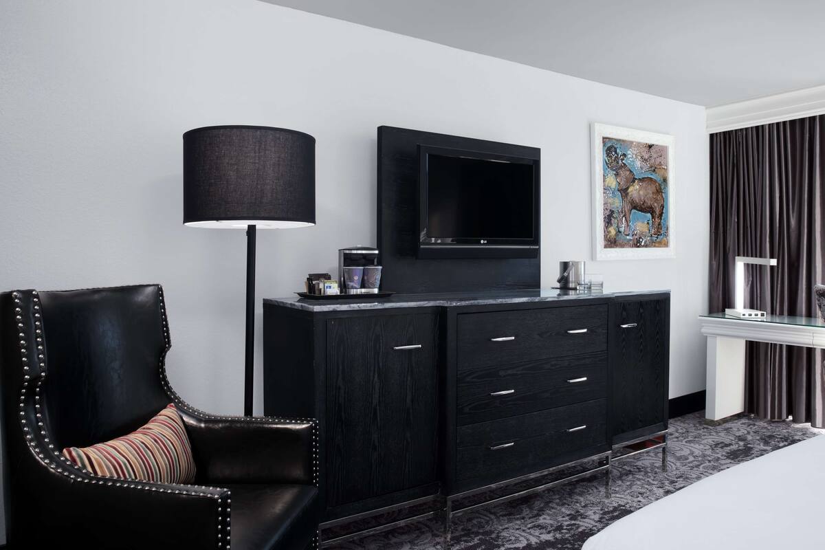 A modern hotel room with a black leather chair, a large flat-screen TV, a black cabinet, and a painting on the wall.