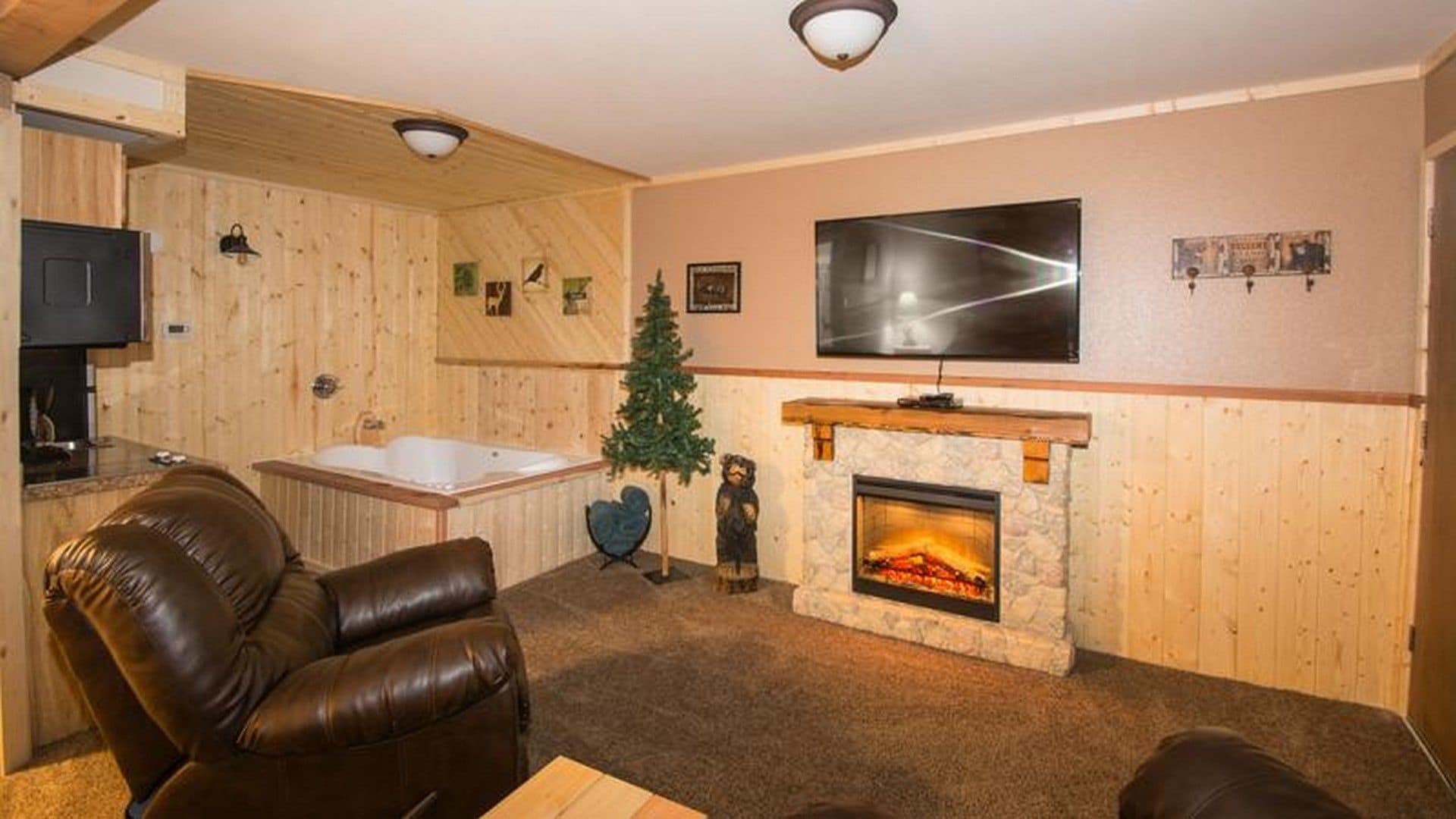 A cozy living room with a fireplace, a large flat-screen TV, a wooden wall, and a leather sofa.