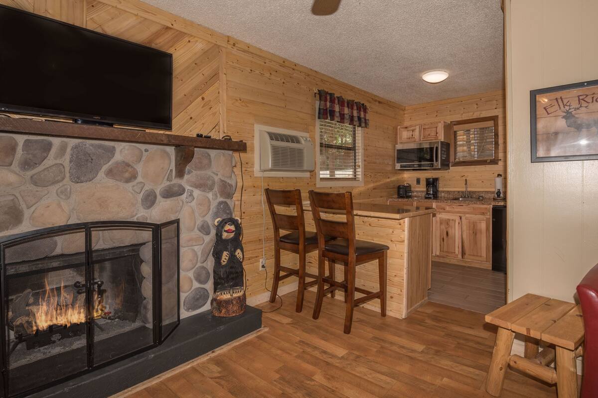 A cozy cabin interior with a stone fireplace, wooden walls, a kitchen with a microwave, and a red leather chair.