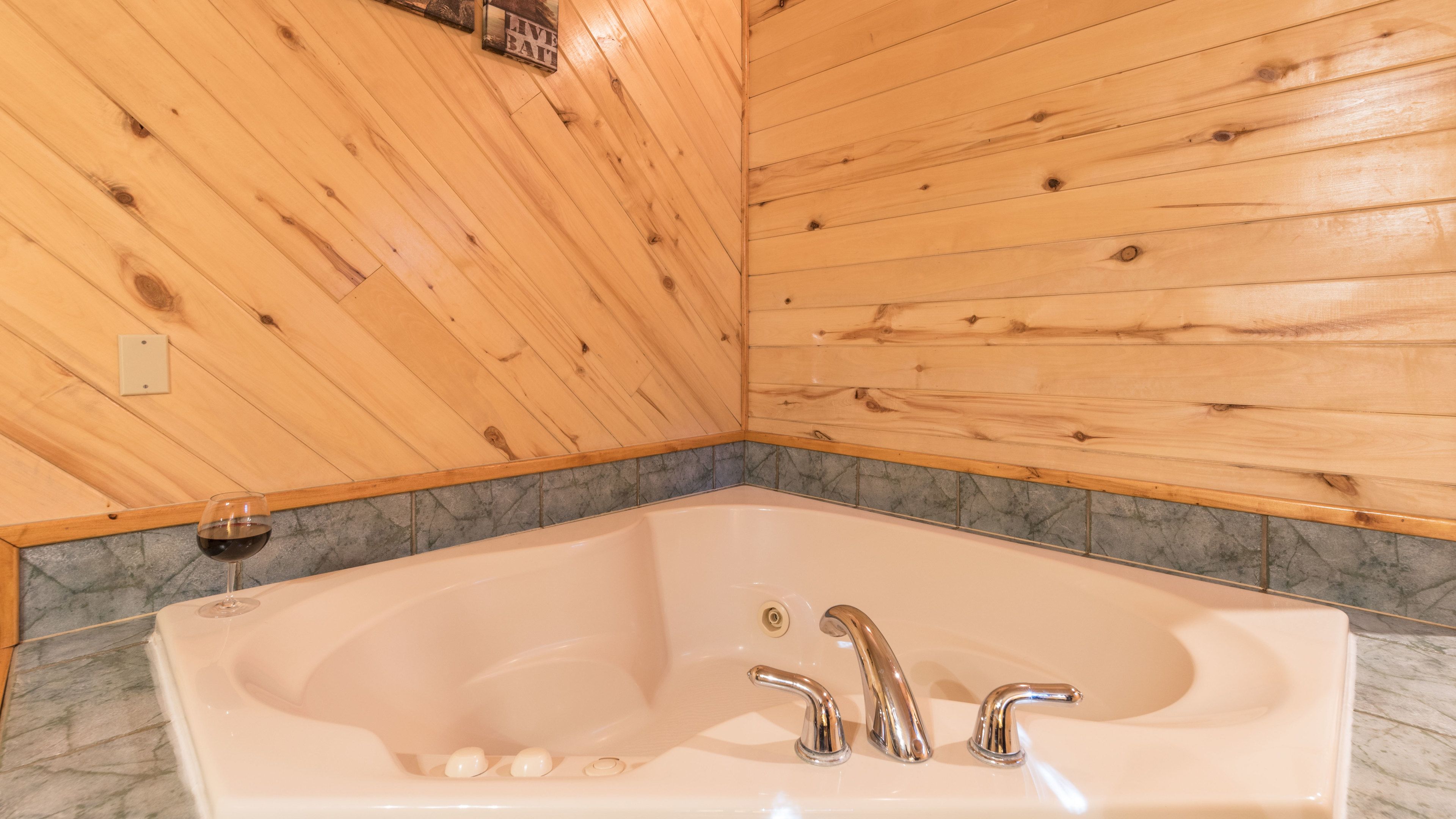 A wooden cabin interior with a large bathtub, marble-tiled walls, and a wooden ceiling.