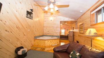 A cabin interior with a wooden interior, a brown leather sofa, a ceiling fan, a bathtub, and a lamp.