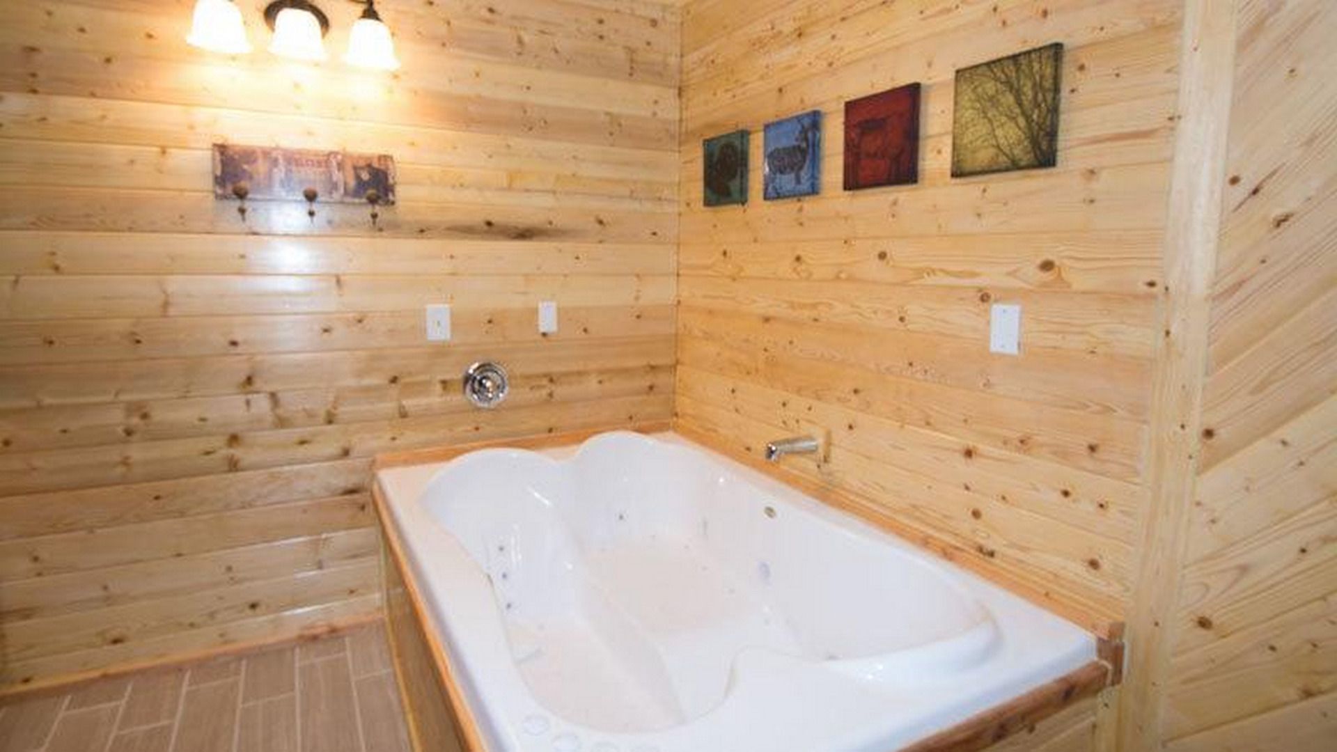 A wooden cabin bathroom with a bathtub, wooden walls, and three framed pictures.