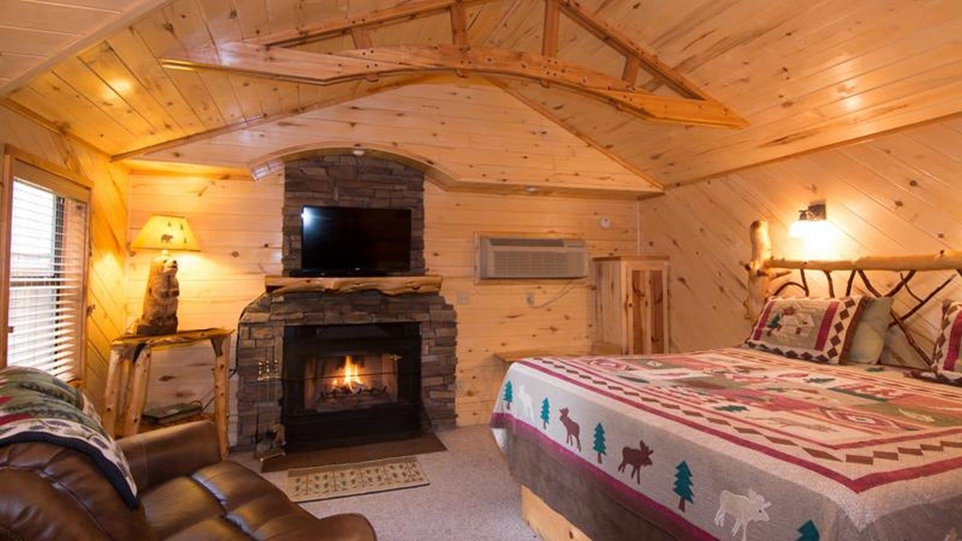 A cozy log cabin bedroom with a fireplace, a bed, and a leather chair.