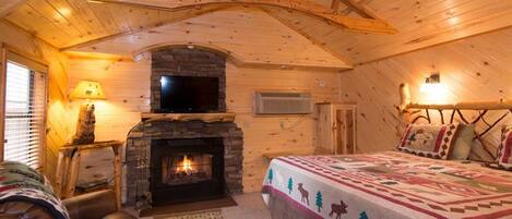 A cozy log cabin bedroom with a fireplace, a bed, and a leather chair.