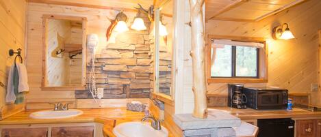 A wooden cabin bathroom with two sinks, a stone accent wall, a mirror, and a window.