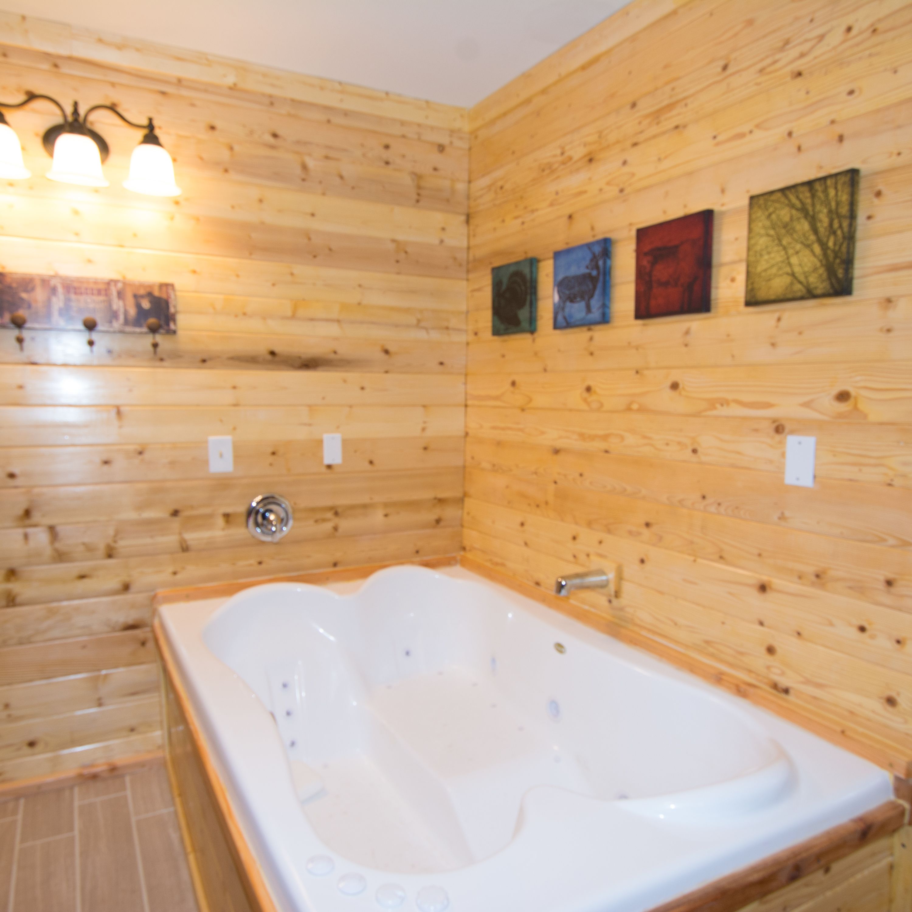 A wooden-paneled bathroom with a large bathtub, wall-mounted lights, and three framed pictures.