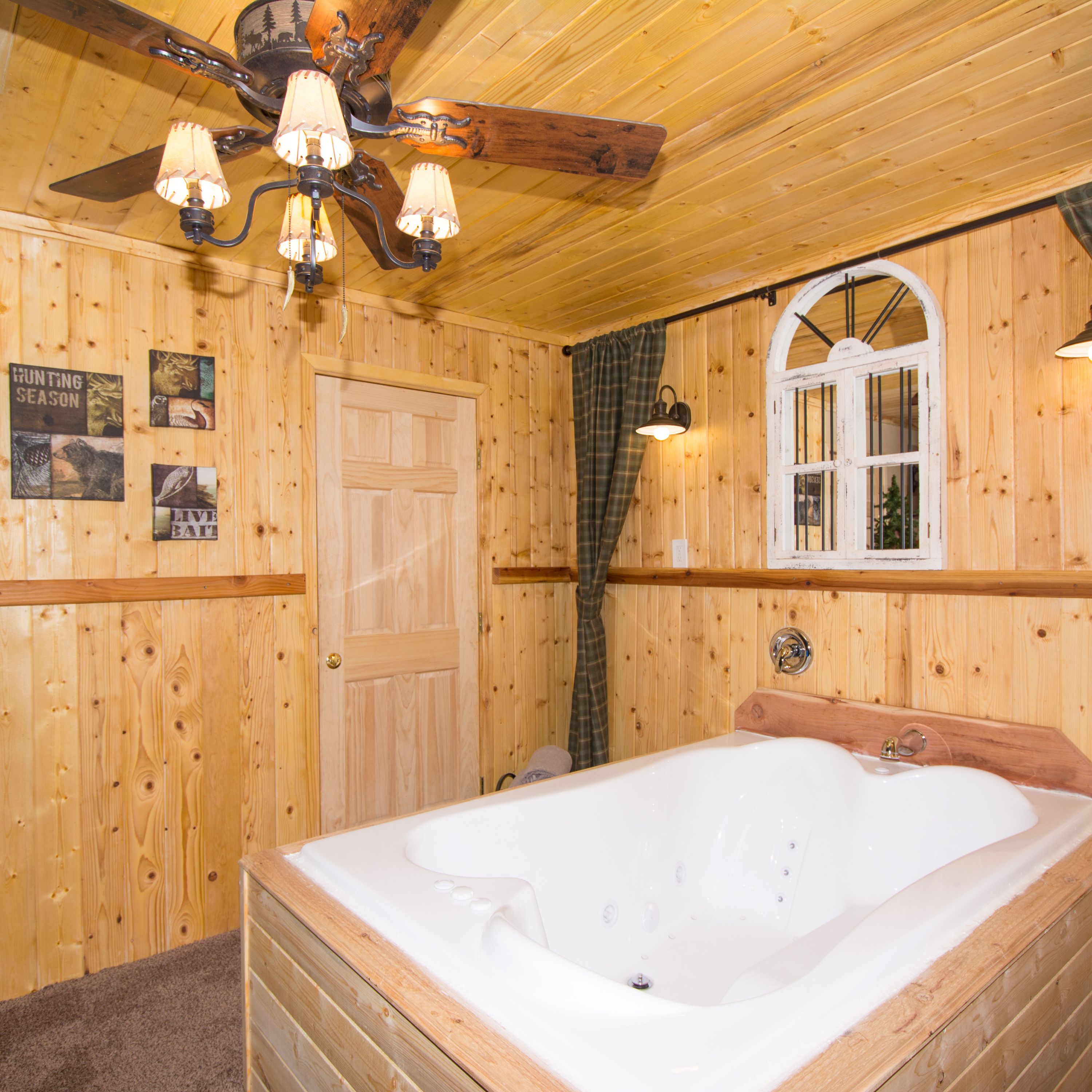 A wooden cabin interior with a large bathtub, a ceiling fan, and wall-mounted lights.