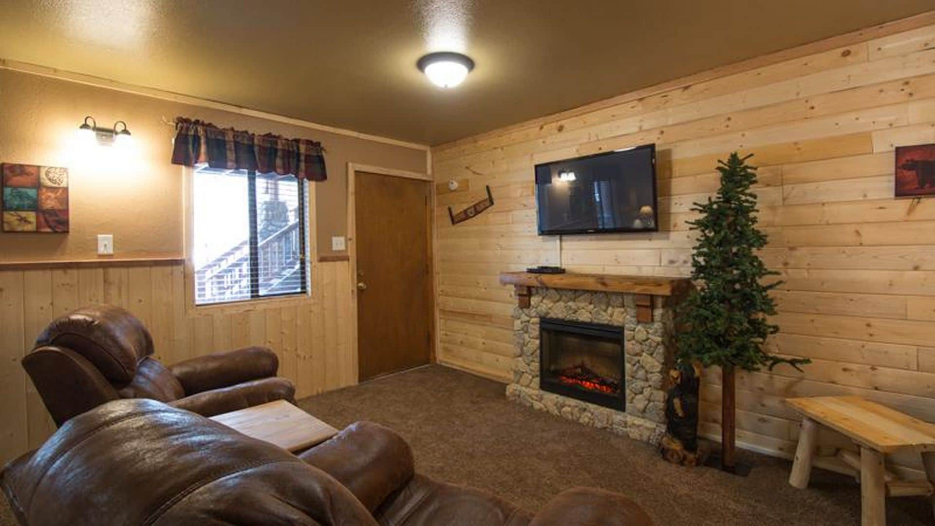 A cozy living room with a stone fireplace, leather sofas, a flat-screen TV, and a Christmas tree.