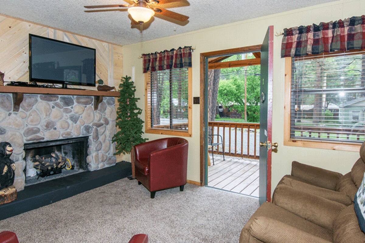 A cozy living room with a stone fireplace, a television, a red armchair, and a door leading to a deck.