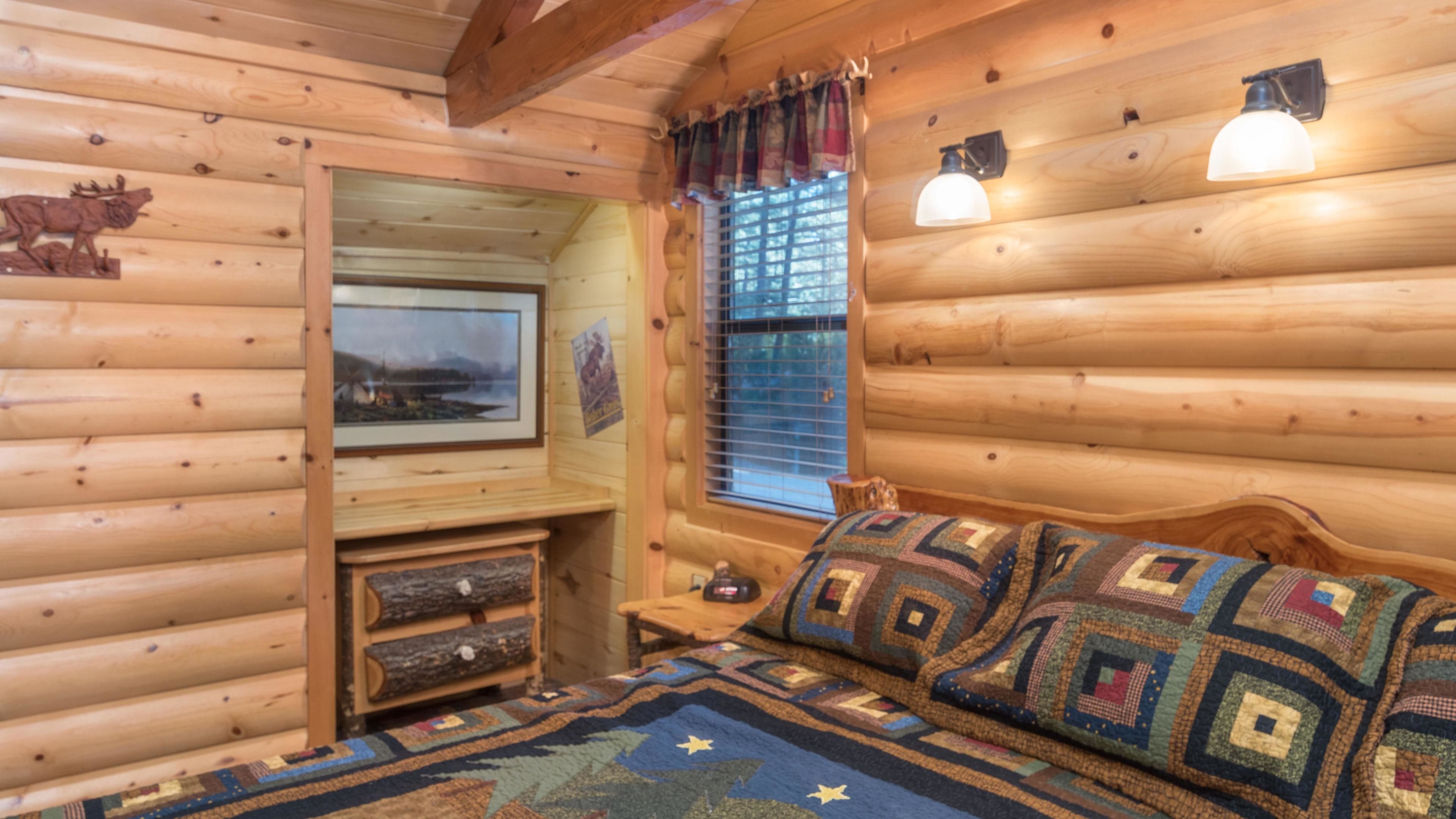 A cozy log cabin room with a bed, a small desk, and a window with curtains.