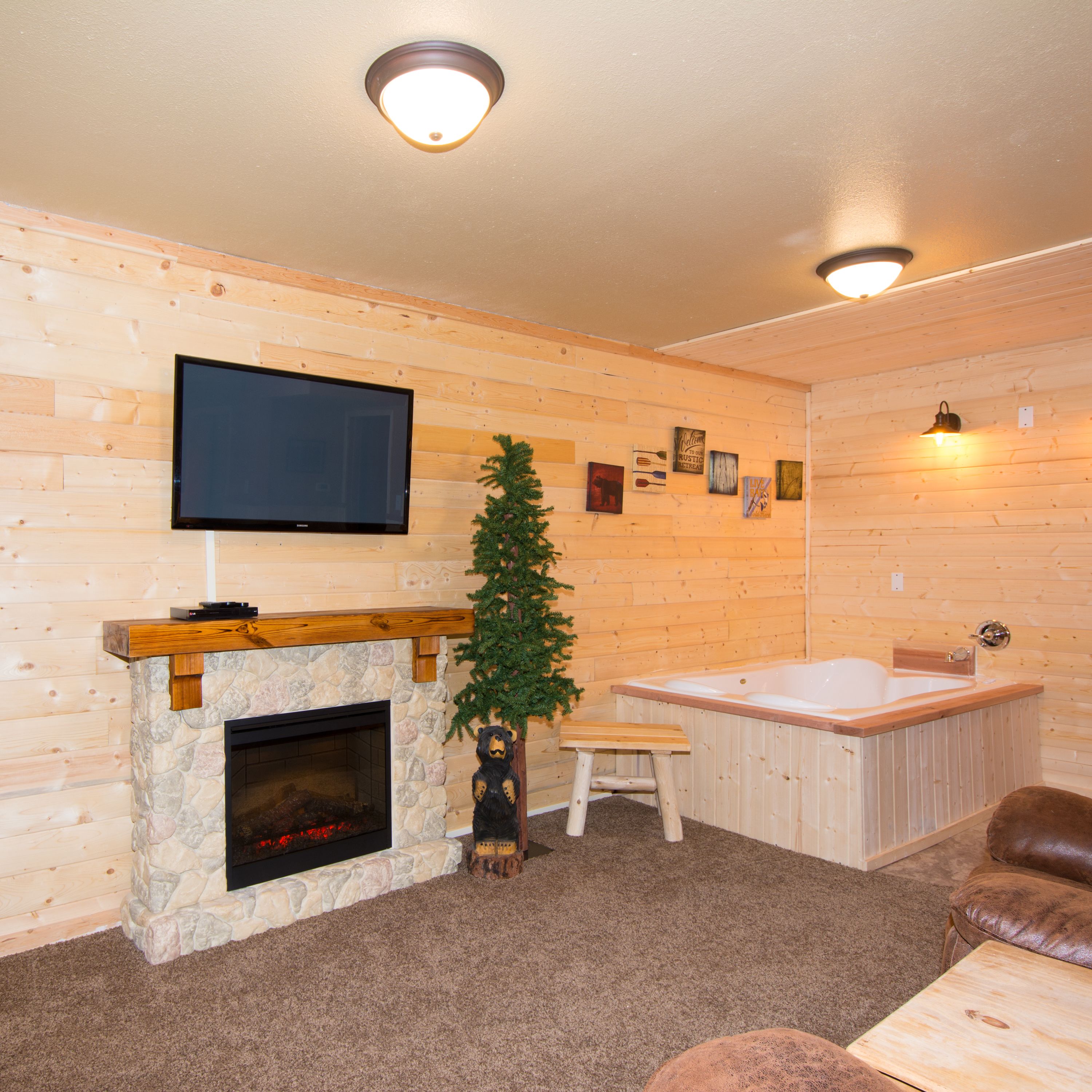 Ein gemütliches Zimmer mit Kamin aus Stein, einem an der Wand befestigten Fernseher, einer Holzbank, einer Bärenstatue, einem Weihnachtsbaum und einer Whirlwanne.