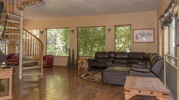Uma sala de estar ampla com escada de madeira, sofá de couro e janelas grandes com persianas.