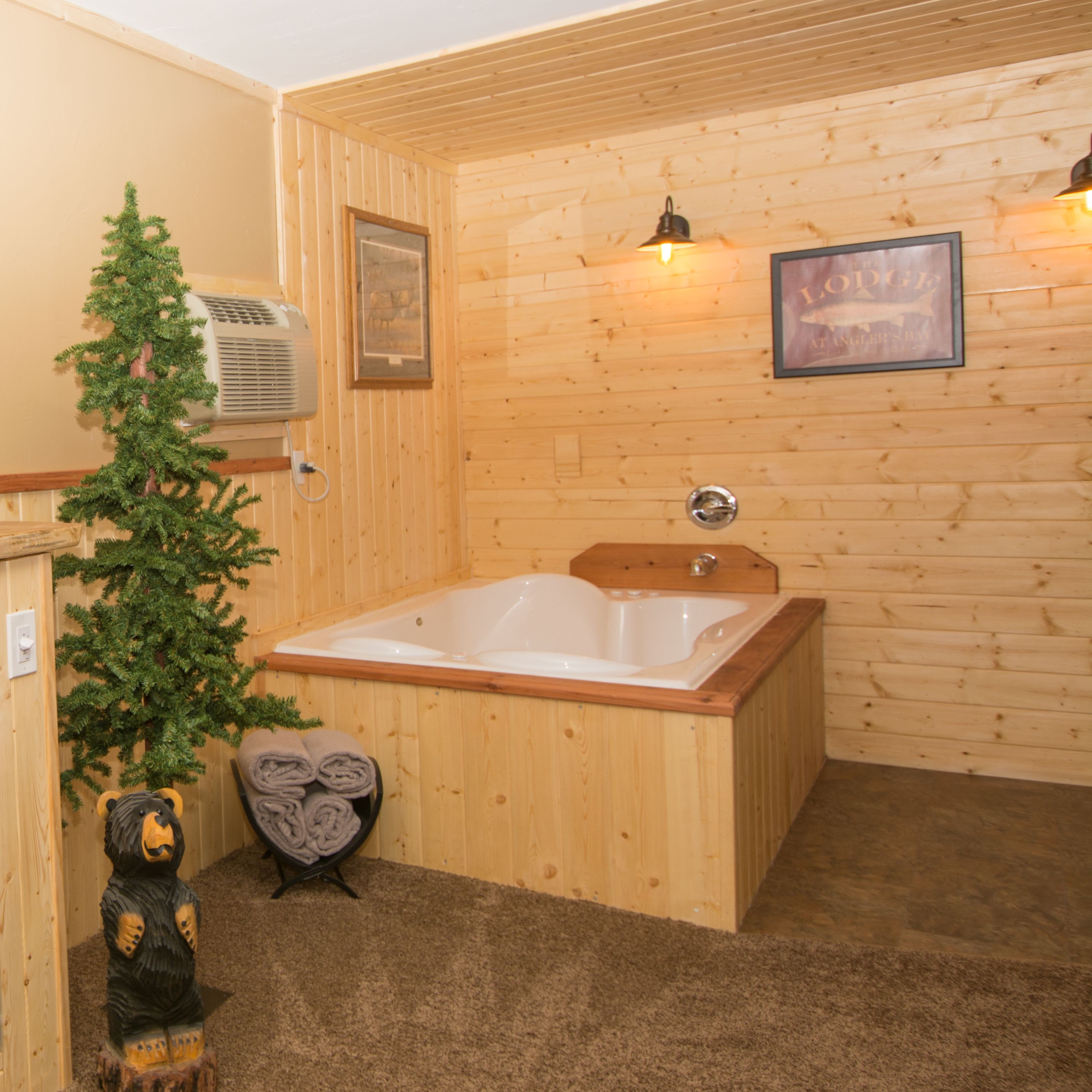 A wooden cabin interior with a wooden bathtub, a small Christmas tree, and a bear statue.