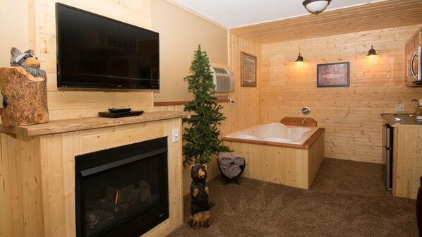 Un interior de madera con chimenea, televisor, un pequeño árbol de Navidad, una bañera y una estatua de oso.