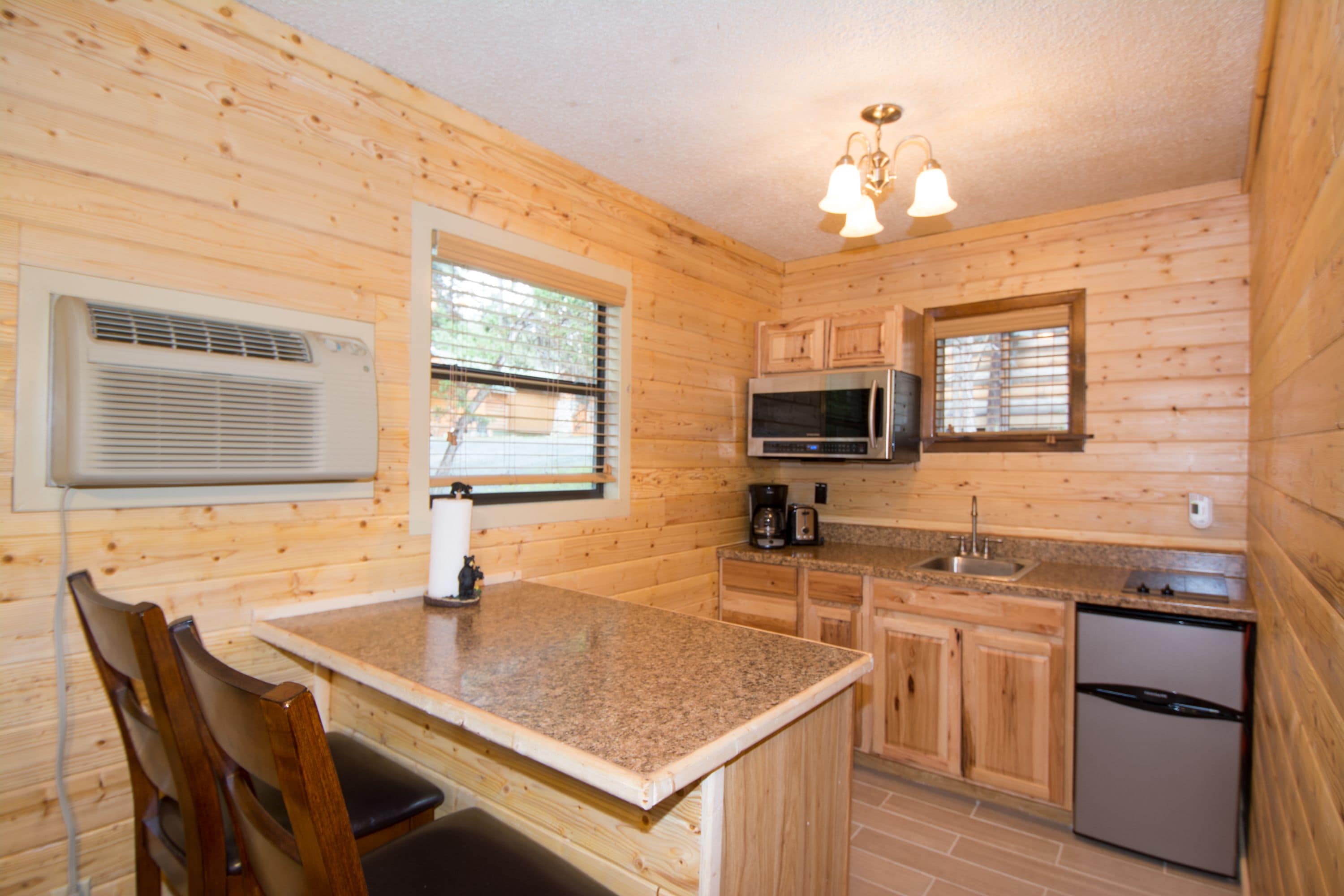 Une cuisine rustique, située dans une cabane en bois, avec des comptoirs en granit, un réfrigérateur en acier inoxydable, un four à micro-ondes et un évier.