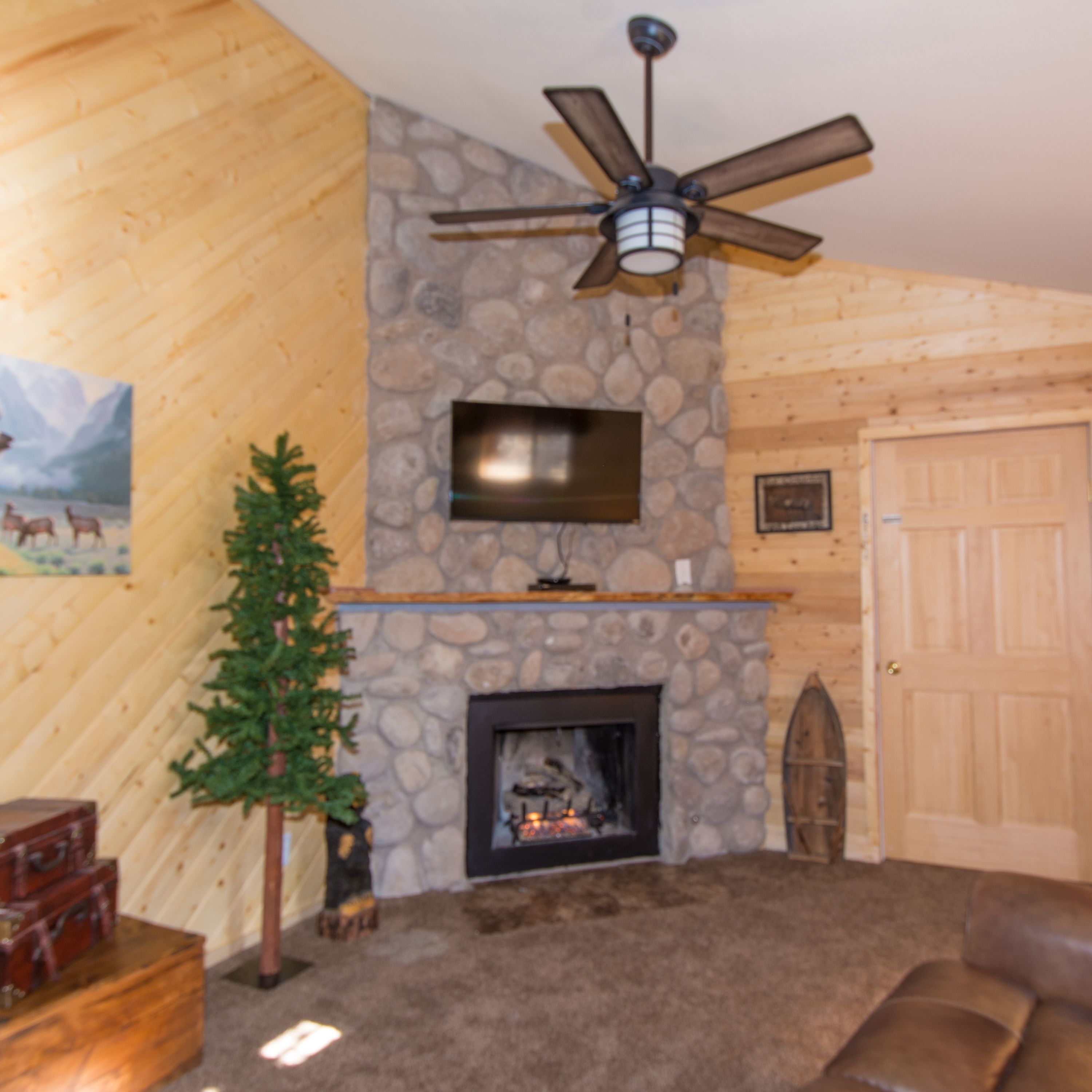 A cozy living room with a stone fireplace, a mounted television, and a ceiling fan.