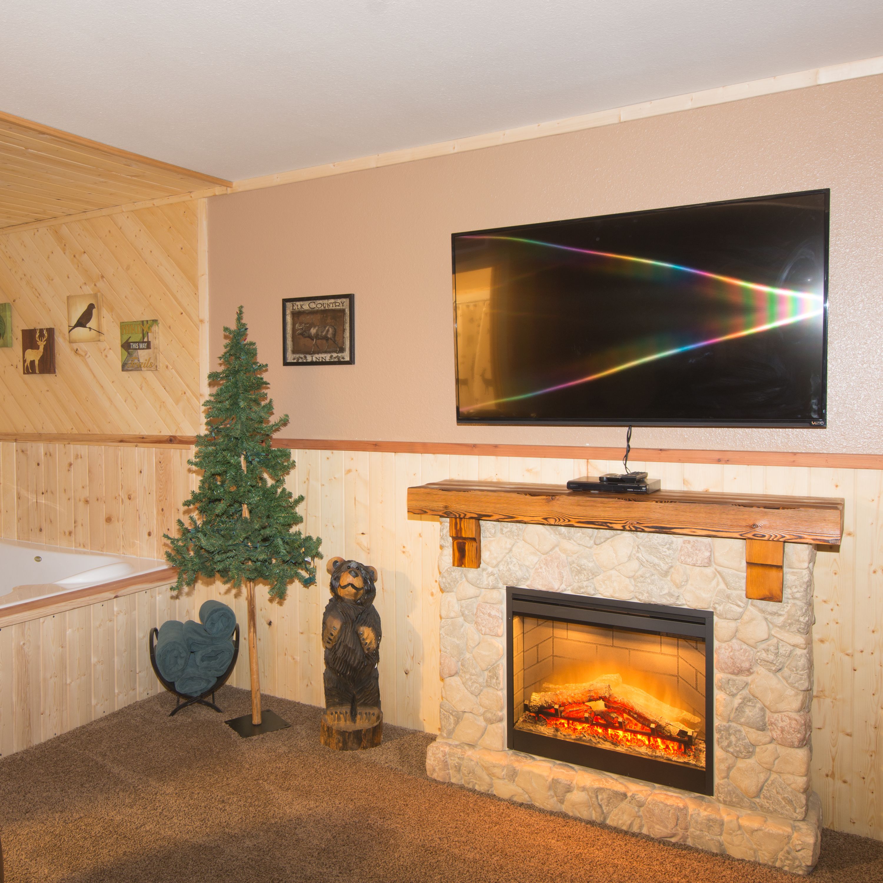 A cozy room with a stone fireplace, a television mounted on the wall, and a small Christmas tree.