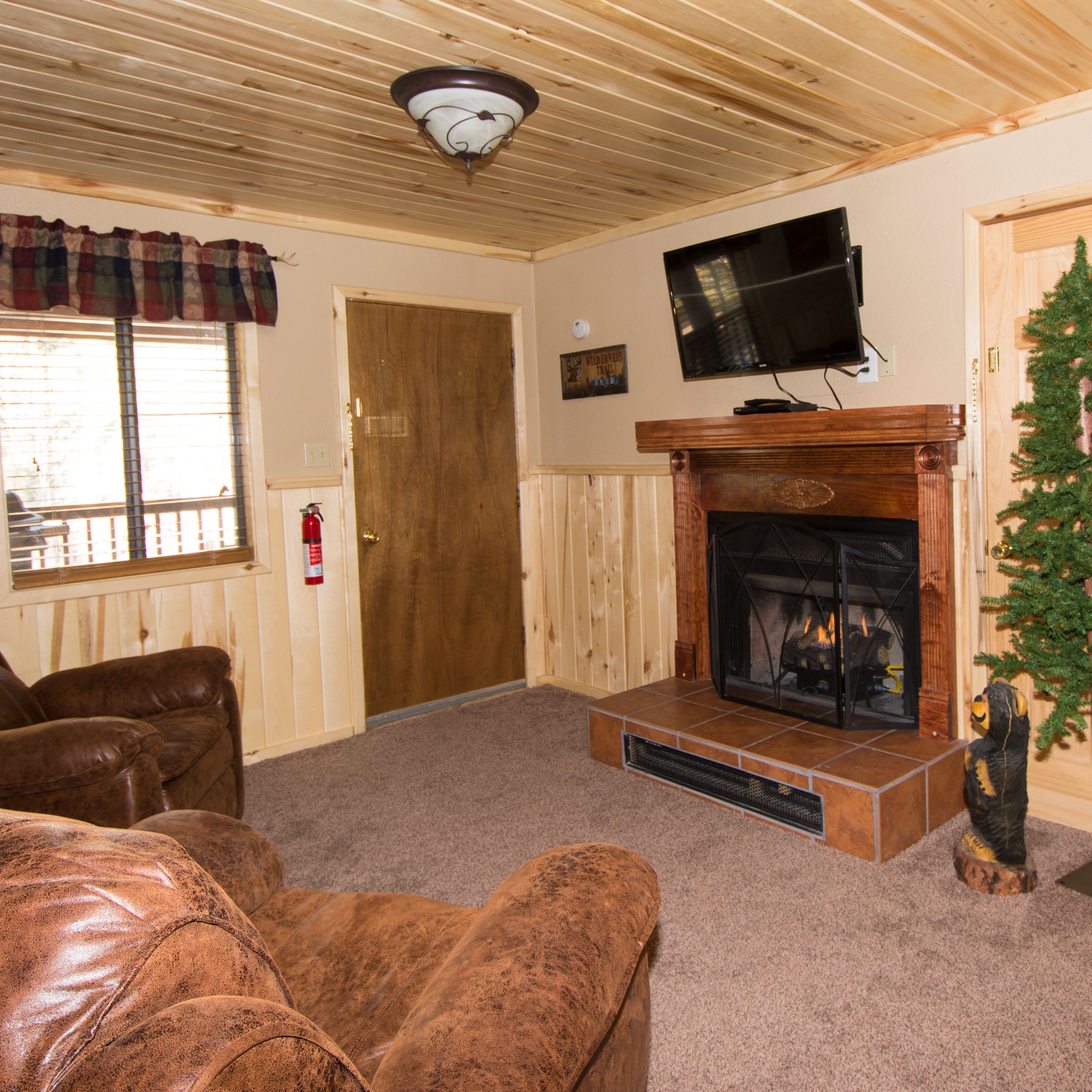 A living room with a fireplace, leather sofas, a television mounted above it, and a Christmas tree.