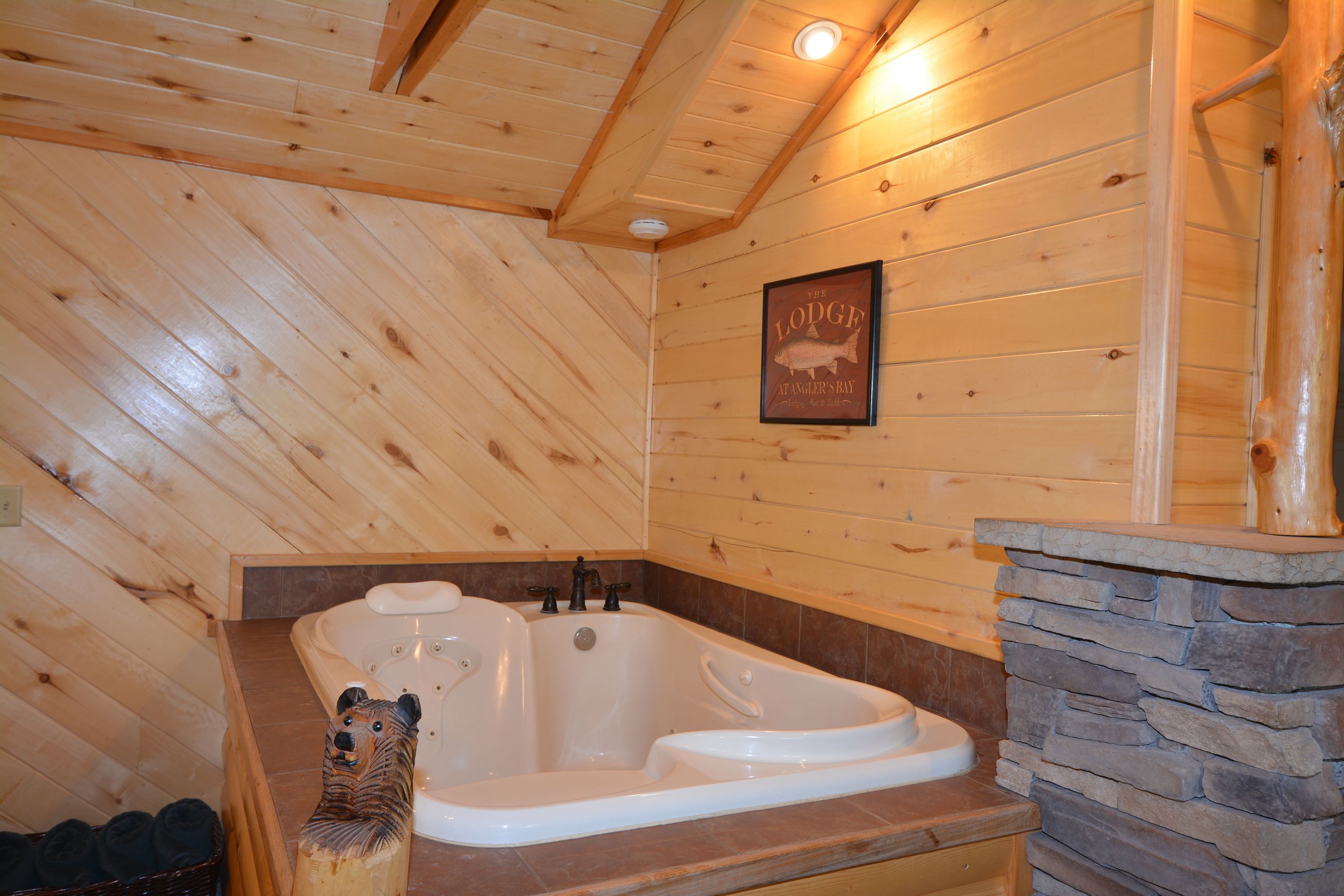 Interior de una cabaña de madera con una bañera grande, paredes de madera y una chimenea de piedra.