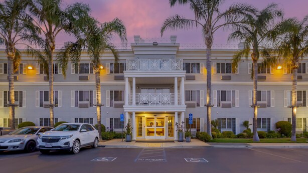 A multi-story hotel with a central entrance, palm trees, and parked cars.