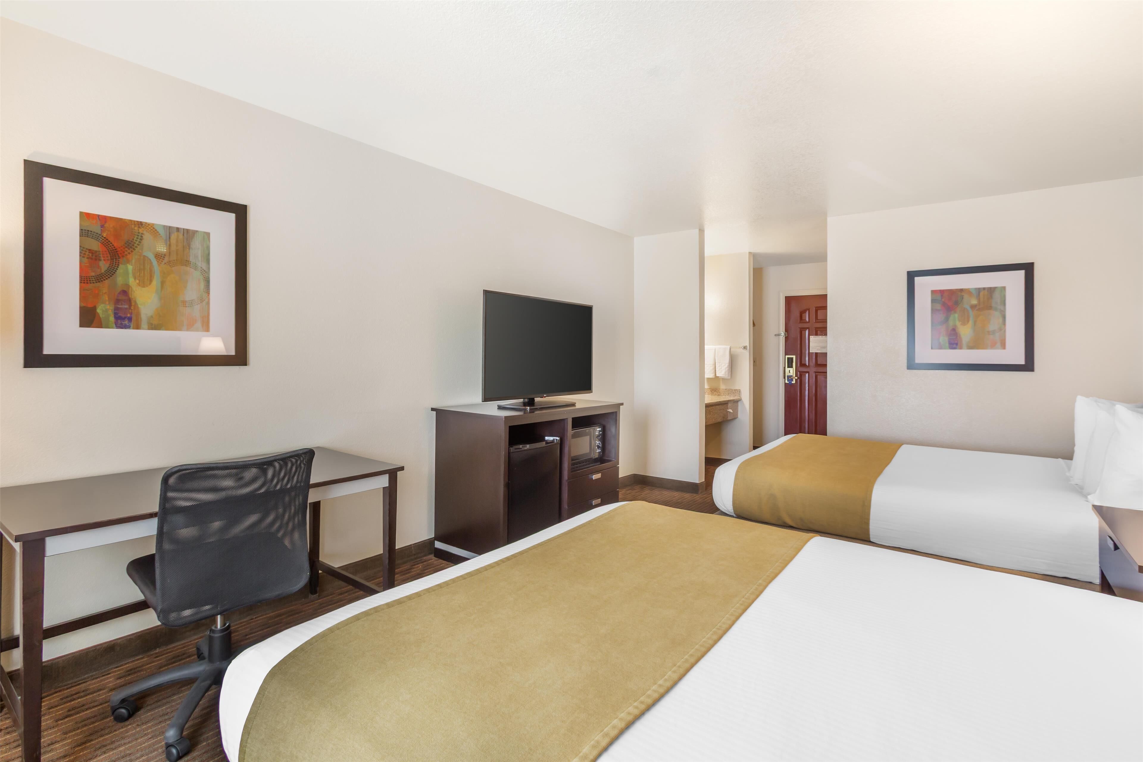 A hotel room with a desk, a television, two beds, and artwork on the walls.