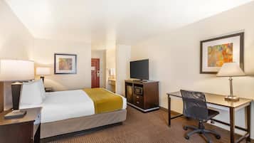 A hotel room with a bed, desk, chair, TV, and artwork on the walls.