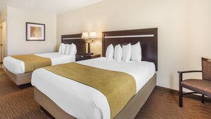 A hotel room with two beds, a nightstand with a lamp, a chair, and a framed picture on the wall.