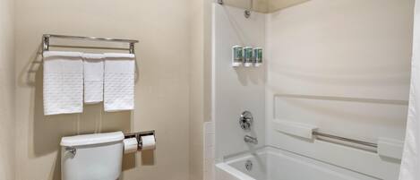 Un baño con inodoro, dos toallas en un perchero, ducha con puerta de cristal y dispensador de papel higiénico.