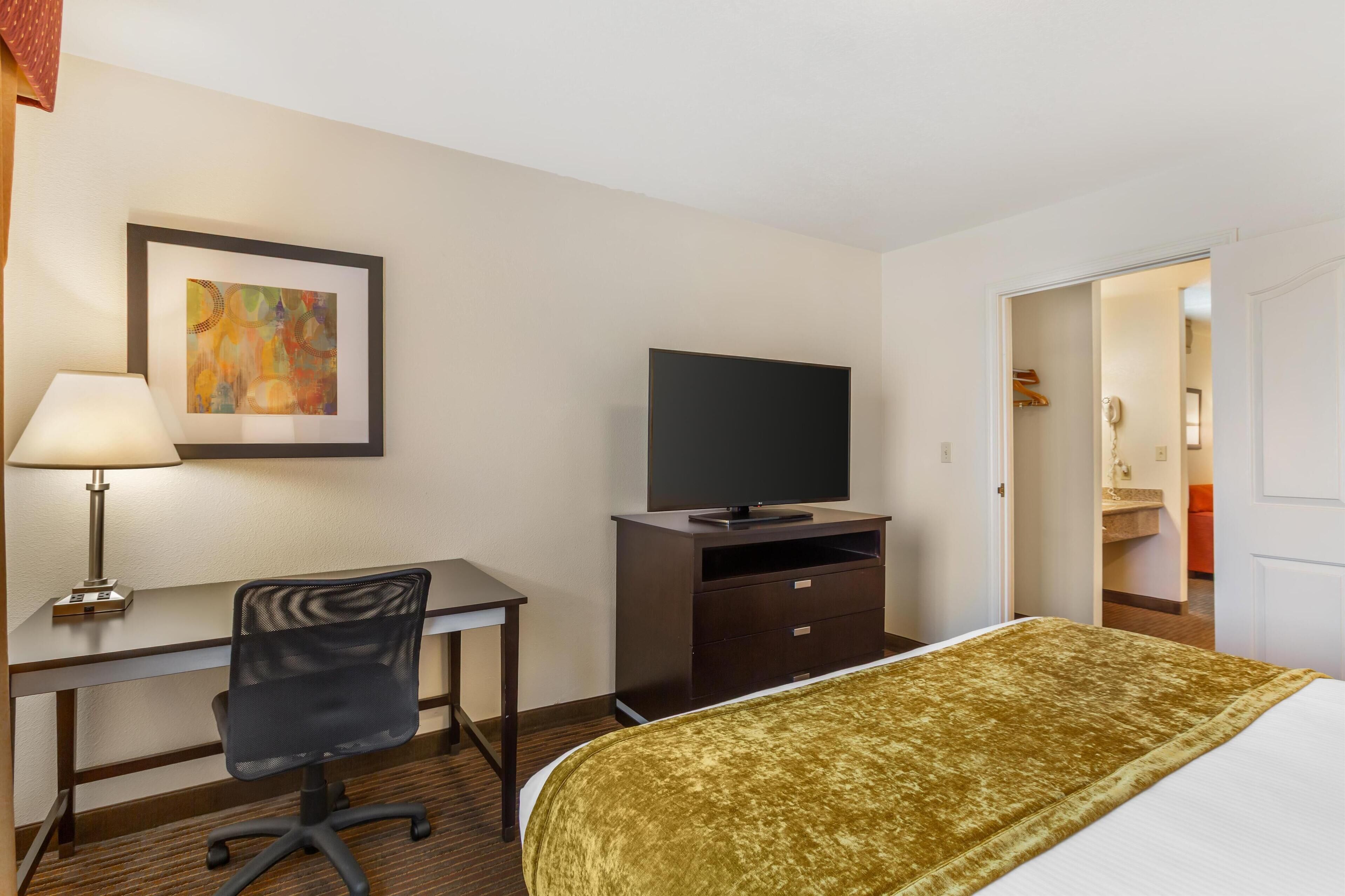 A hotel room with a bed, desk, chair, TV, and a painting on the wall.