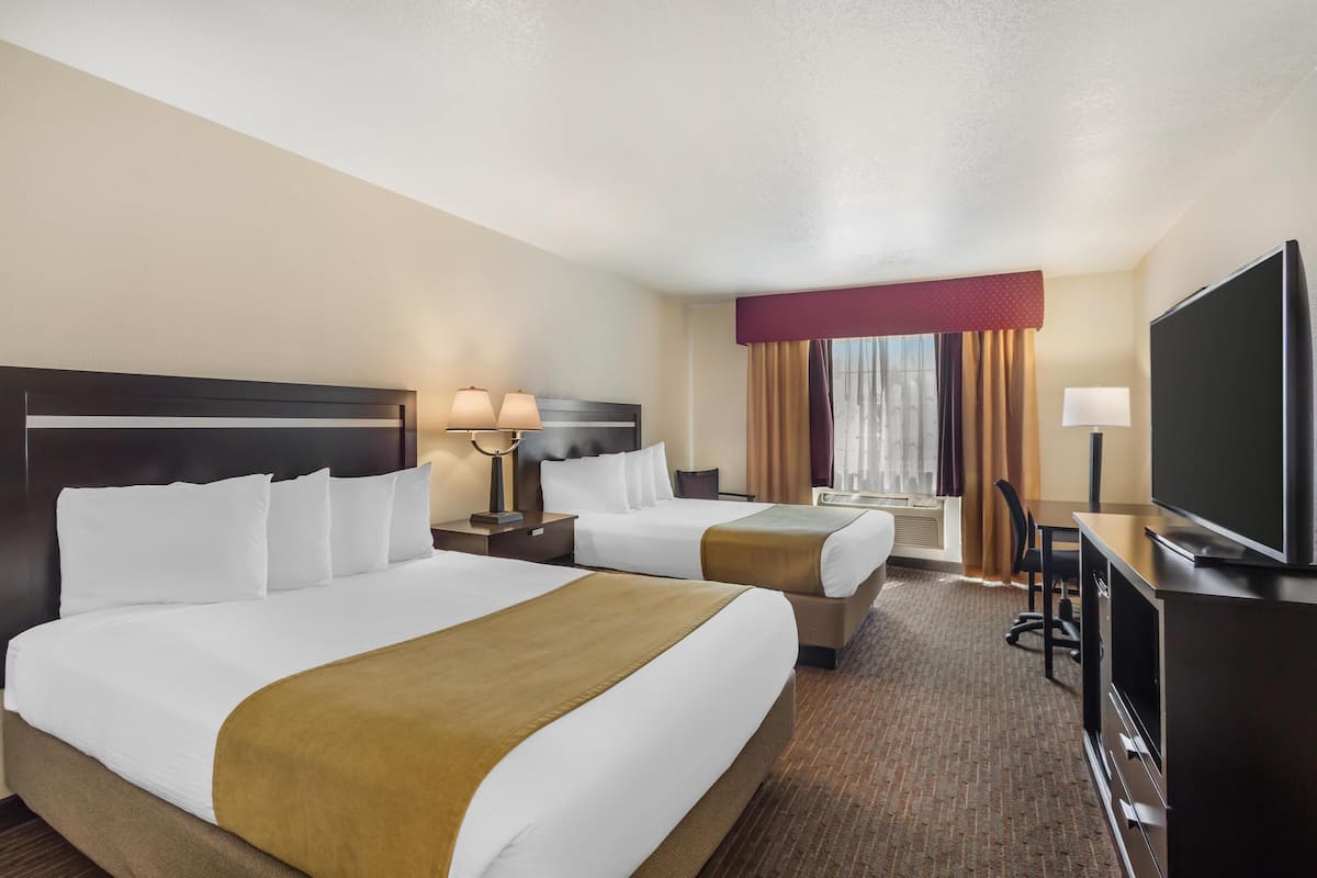 A hotel room with two beds, a TV, a desk, and a window with curtains.