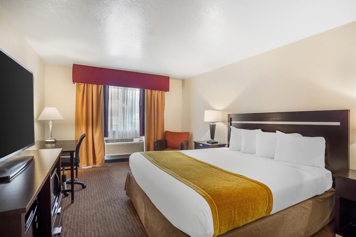 A hotel room with a large bed, a desk with a chair, a TV, and a window with curtains.