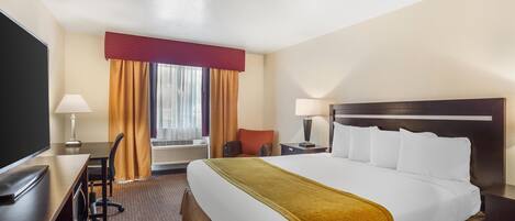 A hotel room with a large bed, a desk with a chair, a TV, and a window with curtains.