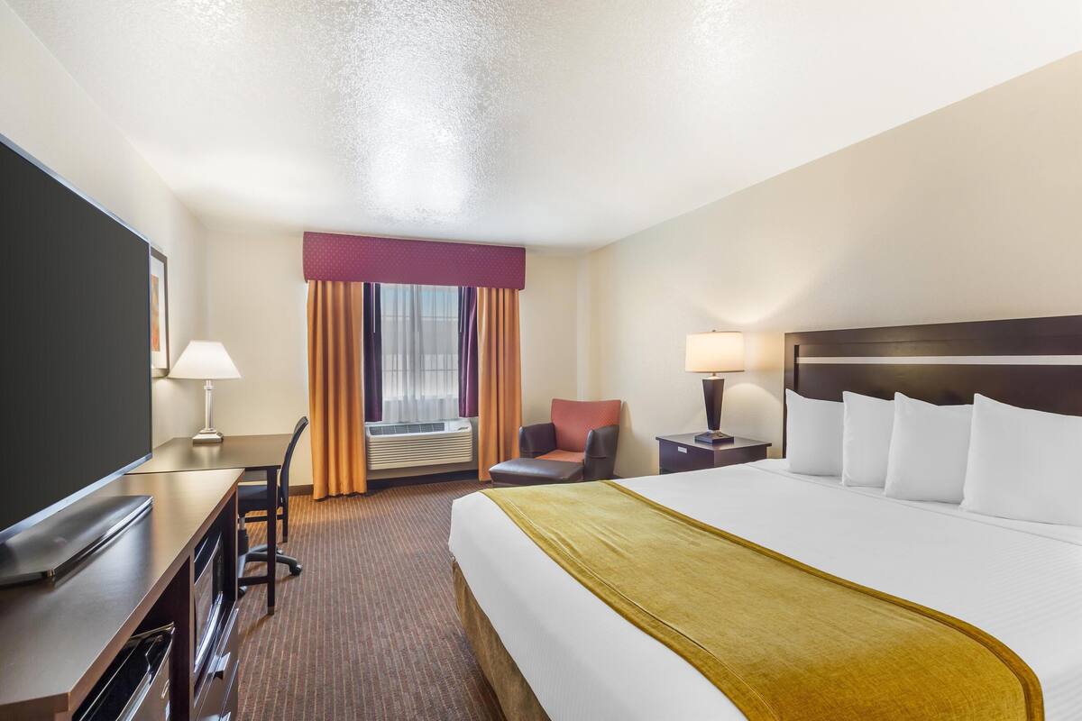 A hotel room with a bed, a desk, a chair, a TV, and a window with curtains.