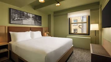 A hotel room with a large bed, a nightstand, a lamp, a window with a view of buildings, and a framed picture on the wall.