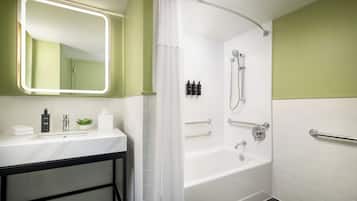 A modern bathroom with a white sink, a mirror with a light, a shower with a handheld showerhead, and a towel rack.